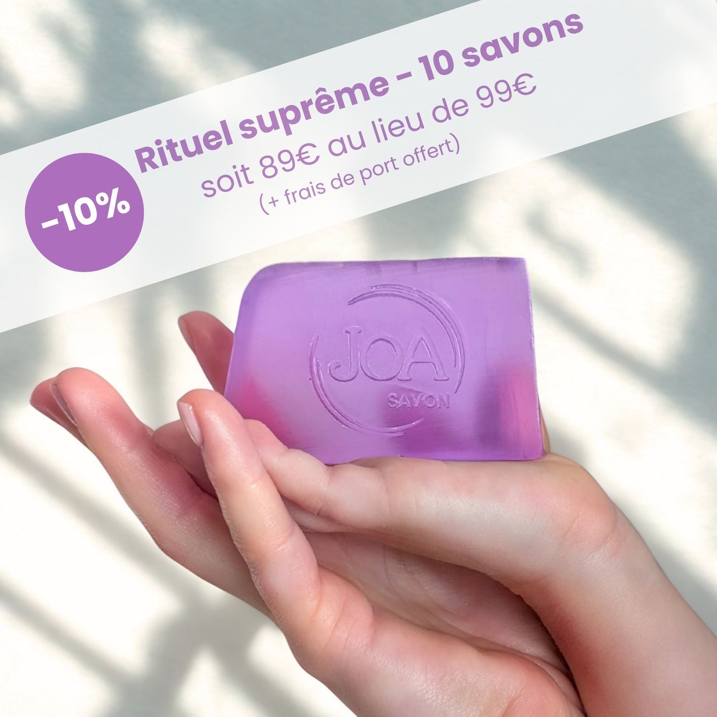 Visuel Joa Savon : Pack 10 savons en promotion (-10 %, 89€ au lieu de 99€), savon violet translucide tenu dans une main, fond clair avec ombres de feuilles.