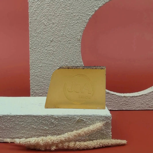 Savon solide Fruit de la Passion Joa jaune doré, posé sur socle blanc texturé avec fond rouge et structure géométrique