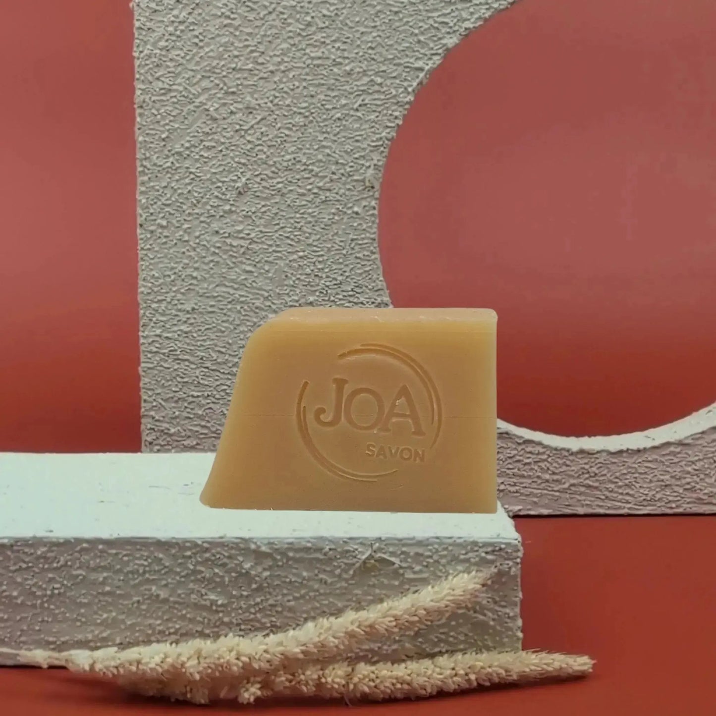 Savon au santal Joa Savon posé sur fond rouge avec décor texturé clair