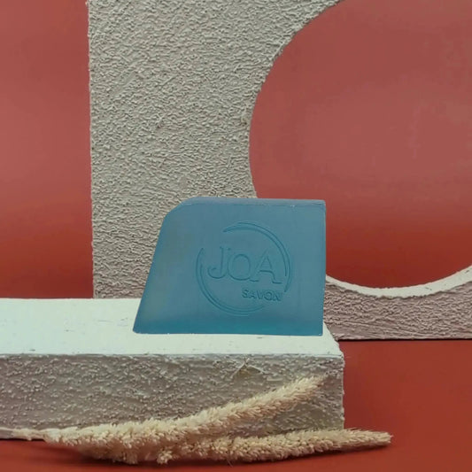 Savon solide Spa de Joa, bleu clair, sur socle blanc avec fond rouge géométrique