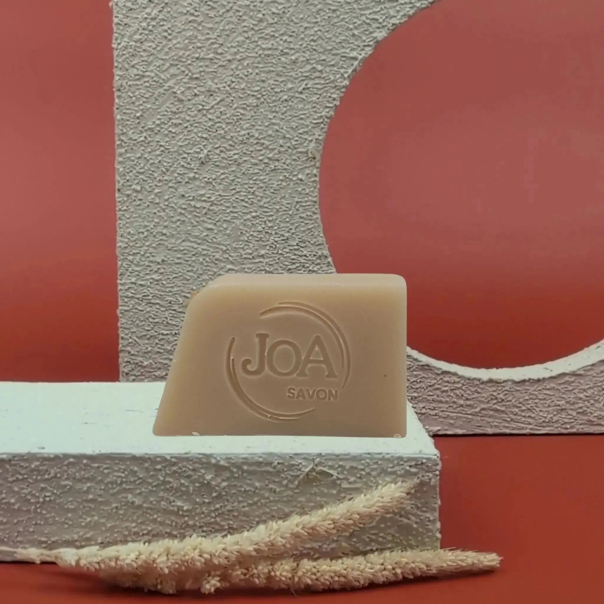 Savon solide Talc de Joa, beige clair, posé sur socle blanc avec fond rouge texturé