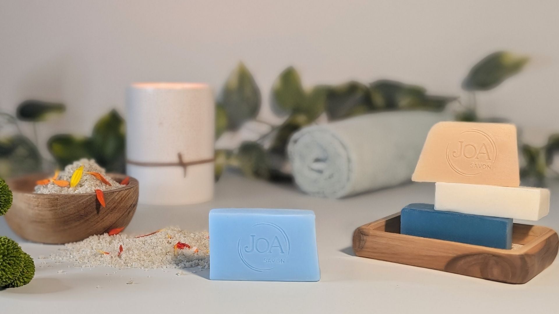 Savons Joa aux couleurs variées – ambiance spa avec sel parfumé et serviette roulée.