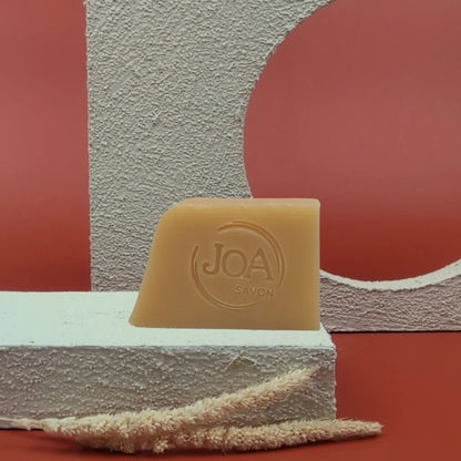 Savon au santal Joa Savon posé sur fond rouge avec décor texturé clair

