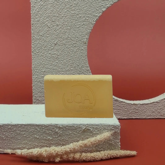 Savon au soufre Joa Savon, posé sur socle blanc, avec fond rouge et décor en relief

